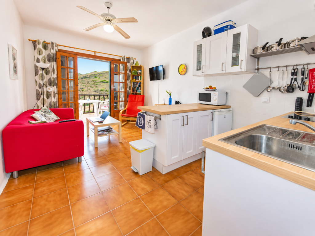 Cocina completamente equipada integrada con salón y acceso al balcón en un apartamento de temporada en Playas de Fornells.