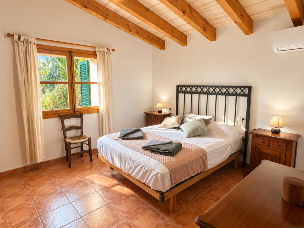 Dormitorio doble de estilo mediterráneo con vigas de madera y aire acondicionado en una casa vacacional en Sóller, Mallorca.