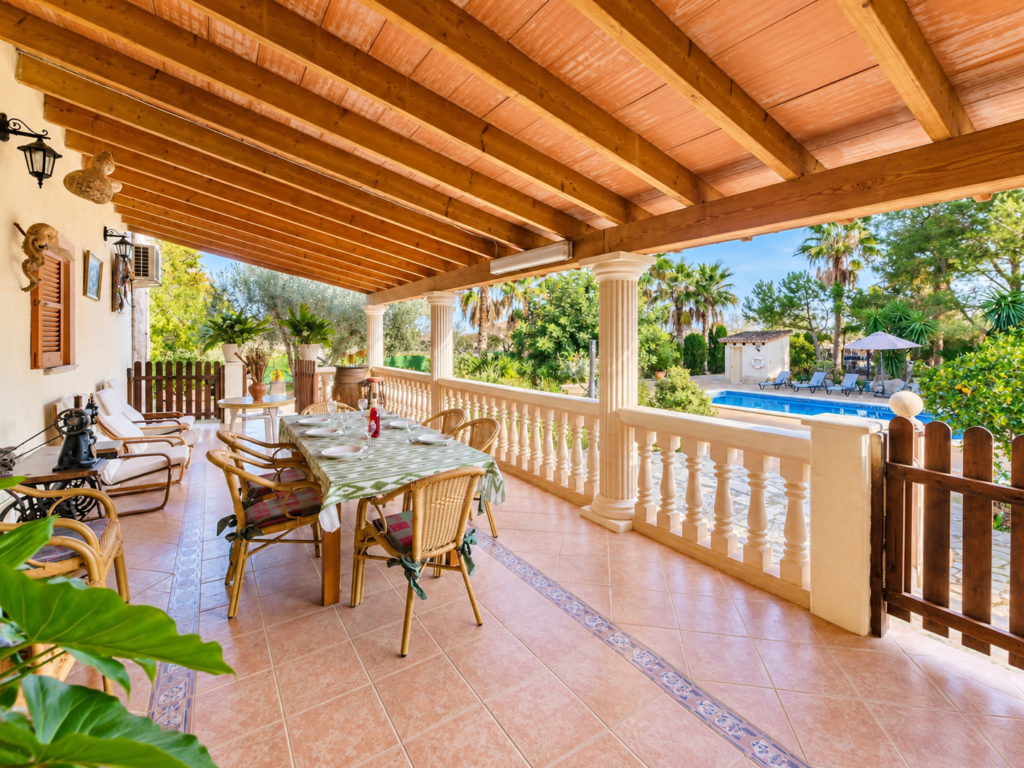 Porche cubierto con gran mesa para comer al aire libre y vistas a la piscina privada de una villa en Lloseta, Mallorca.