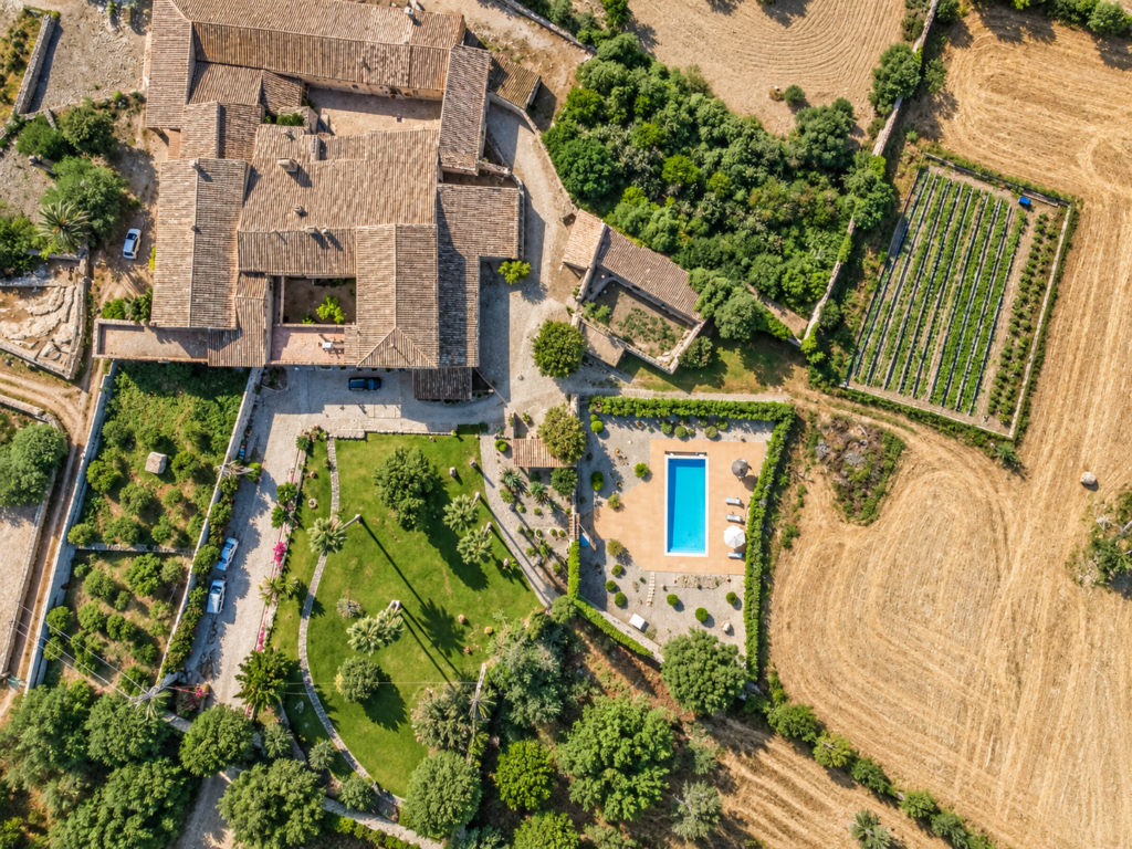 Vista aérea de una finca vacacional en Mallorca con piscina privada, jardines y entorno rural rodeado de campos.