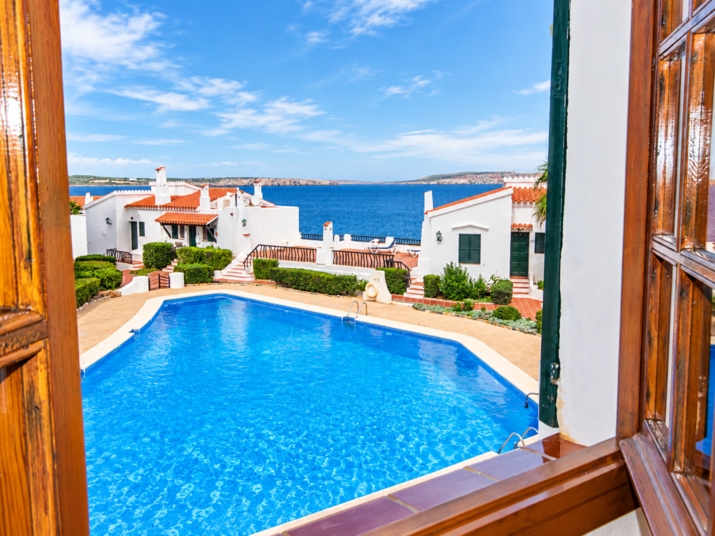 Piscina comunitaria con solárium y vistas al mar en una tranquila urbanización de Playas de Fornells, Menorca.